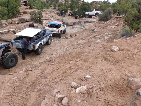 1984 Ford Bronco - Multiple off-road vehicles navigate a challenging rocky and dirt trail in a desert landscape.