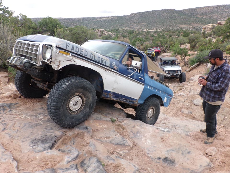 Blue and white Ford Bronco with 'Faded Glory' on the side, navigating a rocky trail with other vehicles behind it