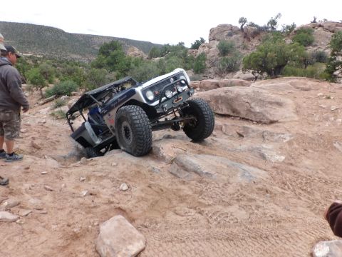 1984 Ford Bronco - Off-road vehicle with large tires navigating rocky terrain, driver visible.