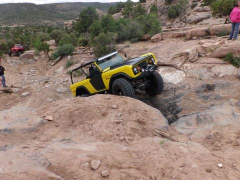 1984 Ford Bronco - Yellow Ford Bronco tackling a challenging off-road course, with another vehicle visible in the distance.