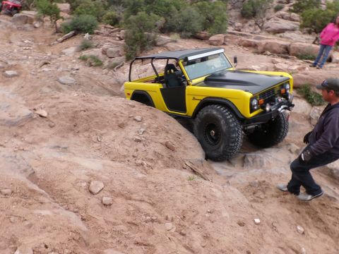1984 Ford Bronco - A yellow Ford Bronco tackles a challenging off-road course with a spotter nearby.