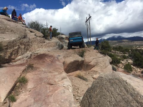1984 Ford Bronco - A blue SUV navigates a steep, rocky terrain with spectators watching from above.
