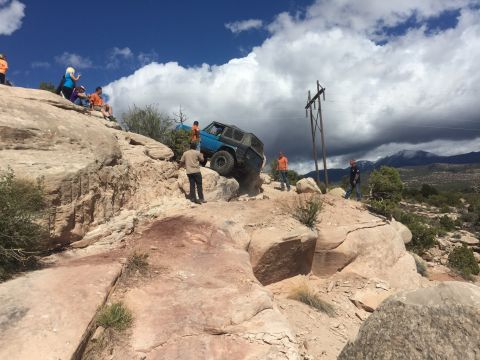 1984 Ford Bronco - A blue off-road vehicle navigates a challenging rocky terrain under a cloudy sky.