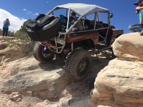 1984 Ford Bronco - A heavily modified off-road vehicle navigates a rocky trail under a clear blue sky.