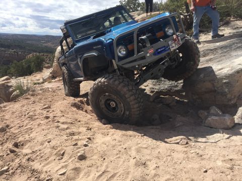 1984 Ford Bronco - A modified blue Ford Bronco navigates a challenging off-road trail with steep, rocky terrain.