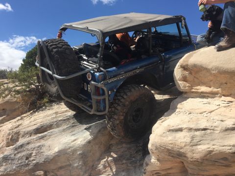 1984 Ford Bronco - This modified SUV navigates a challenging rocky trail under a bright blue sky.