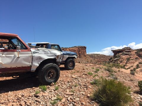 1984 Ford Bronco - Two SUVs are parked on a rocky trail in a desert landscape under a clear blue sky.