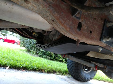 1992 Ford Bronco - Undercarriage view shows a skid plate installed on a vehicle's frame, with a red car visible in the background.