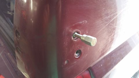1996 Ford Bronco - Close-up of a maroon car body panel with a bolt and screw holes, suggesting a repair or modification.