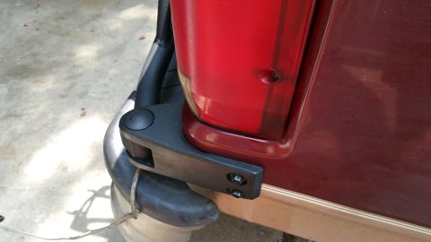 1996 Ford Bronco - Detail of a vehicle's rear bumper and taillight assembly, including a hinge.