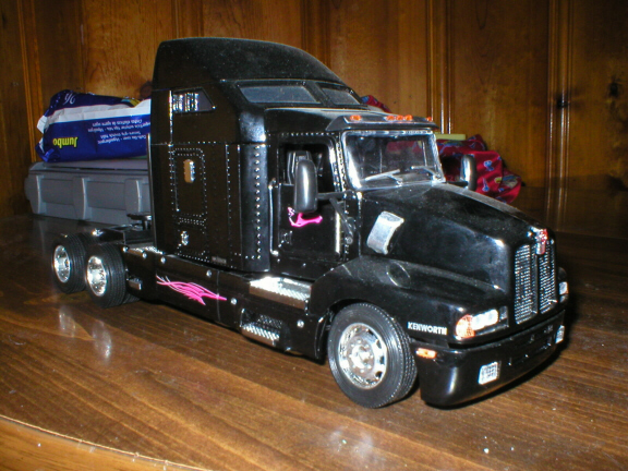 Black Kenworth scale-model semi with pink pinstripe and gray flatbed on a shelf