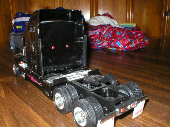 Black scale-model semi truck tractor, rear 3/4 view, on wood surface