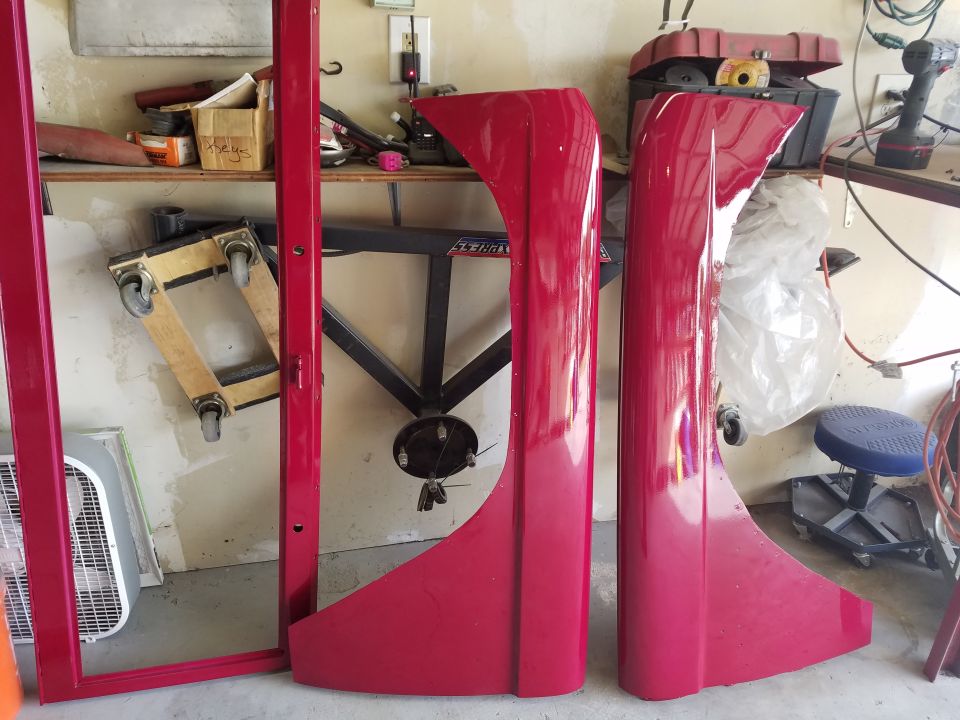 Two red fenders and a red door frame leaning against a wall in a garage