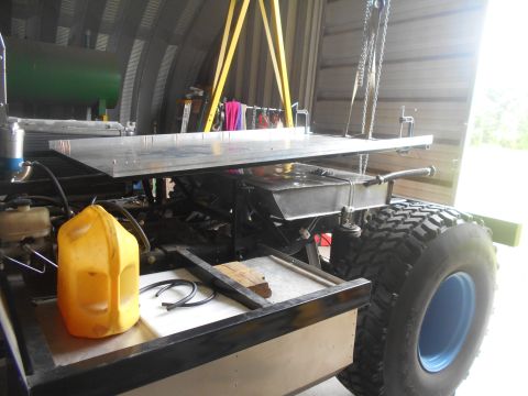 1992 Ford Bronco - A custom vehicle chassis with large off-road tires is suspended by a crane inside a garage.