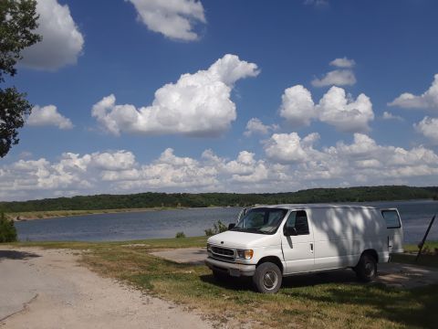 1999 Ford E250 - White 1999 Ford E250 cargo van parked near a lake under a cloudy blue sky.