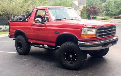 1994 Ford Bronco - This red 1994 Ford Bronco features aftermarket wheels, large tires, and a spare tire mounted on the rear.