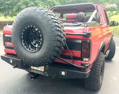 1994 Ford Bronco - This red Ford Bronco shows a rear view with a large spare tire mounted externally and a custom bumper.