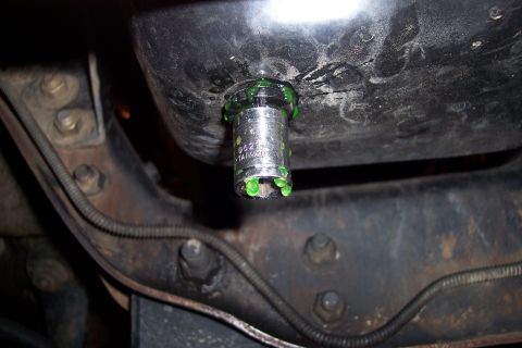 1995 Ford Bronco - A socket wrench is used on an oil drain plug, with green fluid leaking around it.