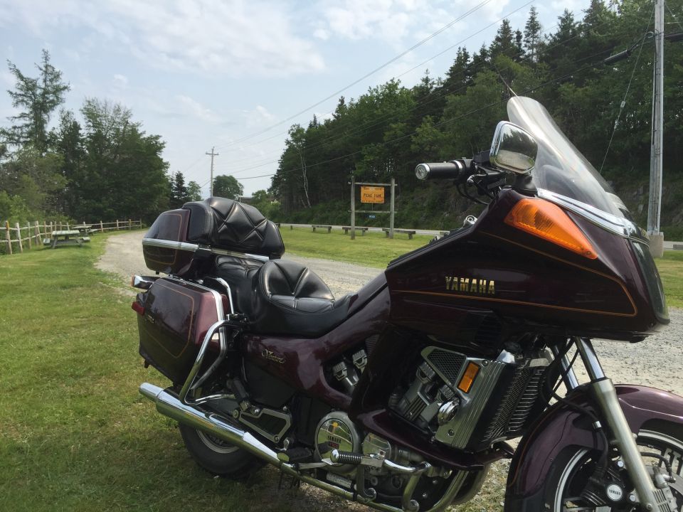 Maroon touring motorcycle parked on a gravel road next to a picnic area