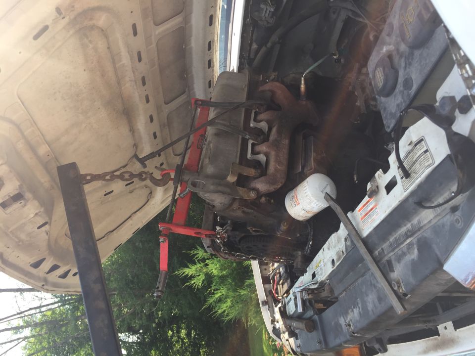 Engine hoist lifting an engine out of a vehicle's engine bay, with an oil filter visible