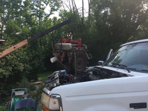 1996 Ford Bronco - An engine is being removed from a white pickup truck using an engine hoist in a residential yard.