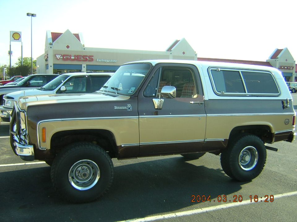 Side view of a brown and tan two-tone SUV parked in a lot. Another car is visible behind it