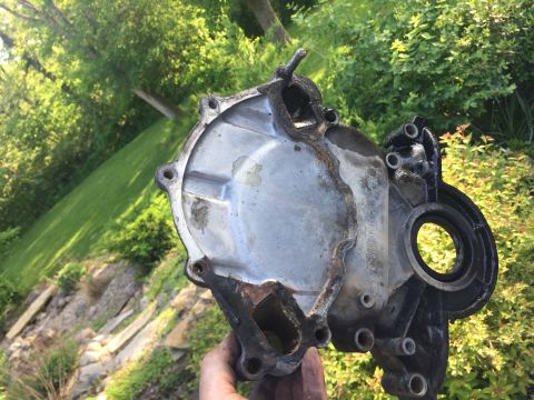 1996 Ford Bronco - A used engine timing cover is held up for inspection against a blurred green background.