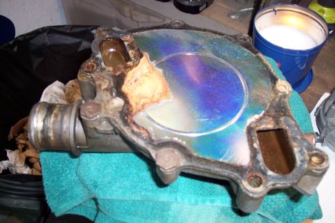 1995 Ford Bronco - This heavily corroded water pump housing shows signs of significant wear and heat damage, with a distinctive iridescent sheen on its surfac…