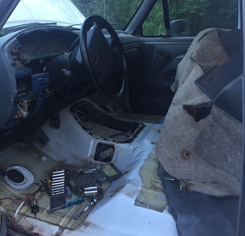 Interior view of a vehicle with the dashboard and seats visible, tools scattered on the floor