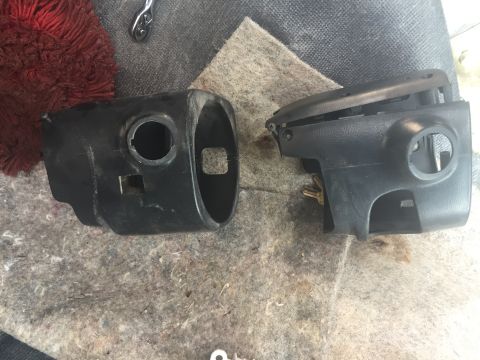 1996 Ford Bronco - Two disassembled plastic steering column shrouds are laid out on a carpeted surface.