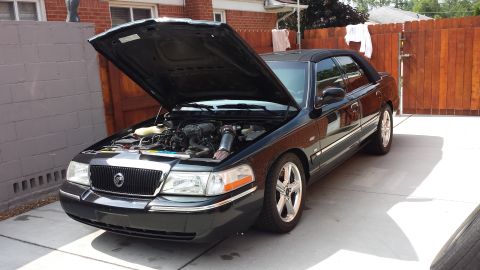2005 Mercury Grand Marquis - Black sedan with hood open, revealing the engine bay and chrome wheels.