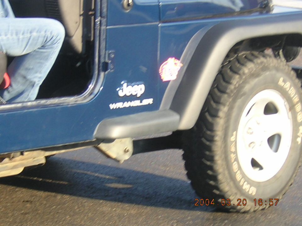 Blue Jeep Wrangler side view, showing door, fender flare, and tire. A person's legs are visible inside