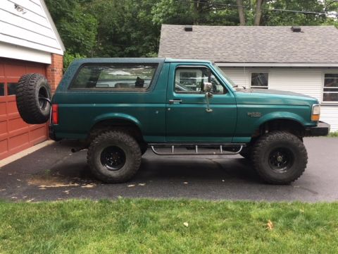 1996 Ford Bronco - This lifted green Ford Bronco is parked in front of a garage with a spare tire on the rear.