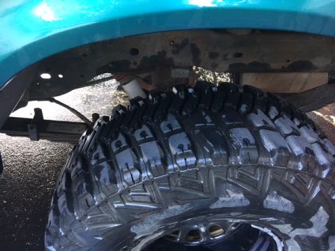 1996 Ford Bronco - The underside of a vehicle, focusing on a large, knobby tire and leaf spring suspension.