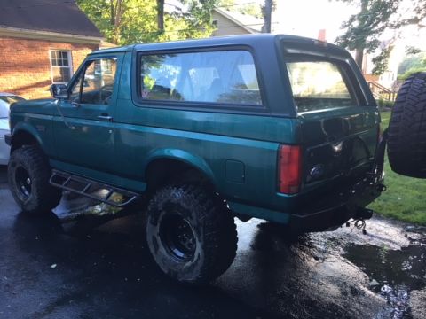 1996 Ford Bronco - A green Ford Bronco is parked on a wet driveway, showing its lifted suspension and off-road tires.