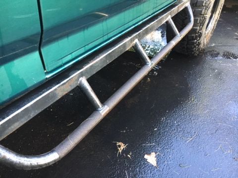 1996 Ford Bronco - Side view of a green vehicle custom metal running boards and a tire.