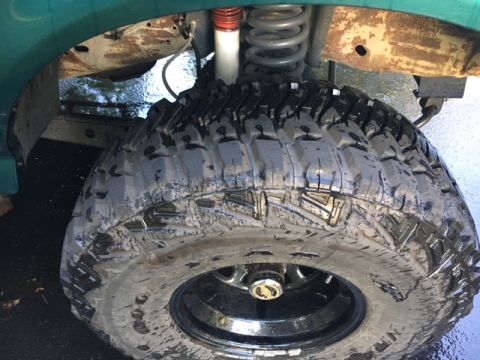 1996 Ford Bronco - Close-up of a muddy off-road tire and suspension parts, showing the wheel and shock absorber.