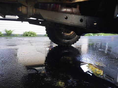 1996 Ford Bronco - A low-angle shot focuses on the undercarriage and a tire of a vehicle parked on wet pavement.