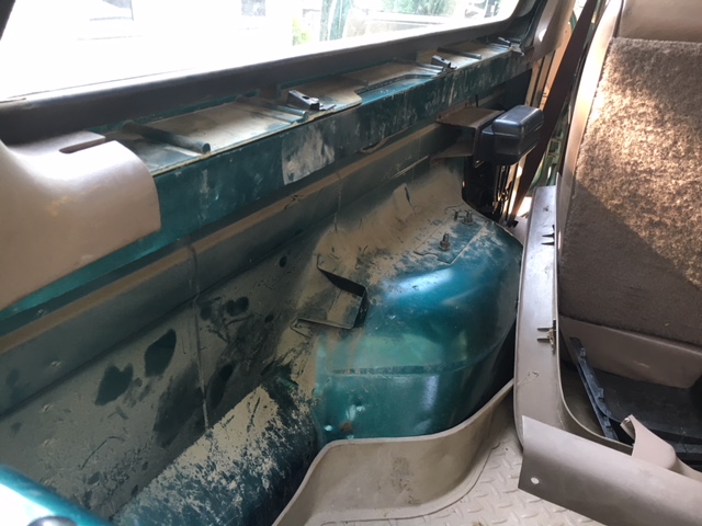 Interior shot of a vehicle's passenger side, showing the green painted metalwork and tan trim panels. Some dirt and dust are visible
