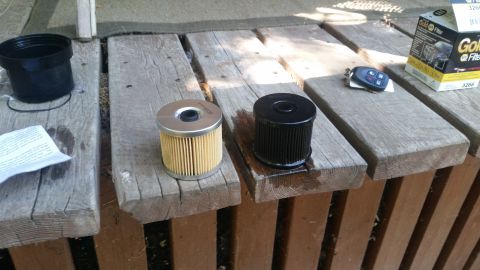 1985 Ford Bronco - Two oil filters, a black cap, car keys, and a box of Gold Filter are laid out on weathered wooden planks.