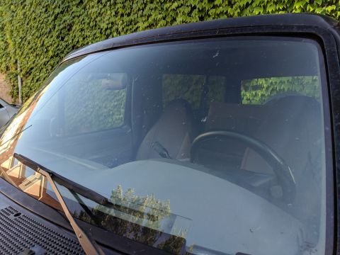 1995 Ford Bronco - The interior of a Ford Bronco is visible through the windshield, with ivy growing on a wall behind it.