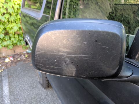 1995 Ford Bronco - Close-up of a worn side mirror on a vehicle, showing numerous scratches.