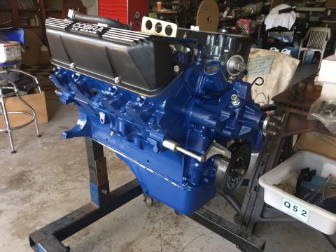 1969 Ford Mustang - A blue V8 engine with black valve covers labeled "COBRA LE MANS" is mounted on an engine stand in a workshop.