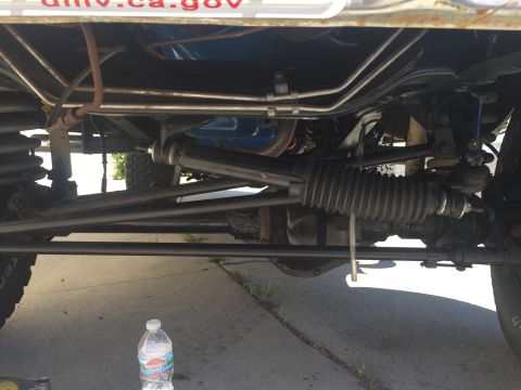 1978 Ford Bronco - Close-up of the steering rack and suspension parts on a vehicle, with a water bottle nearby.