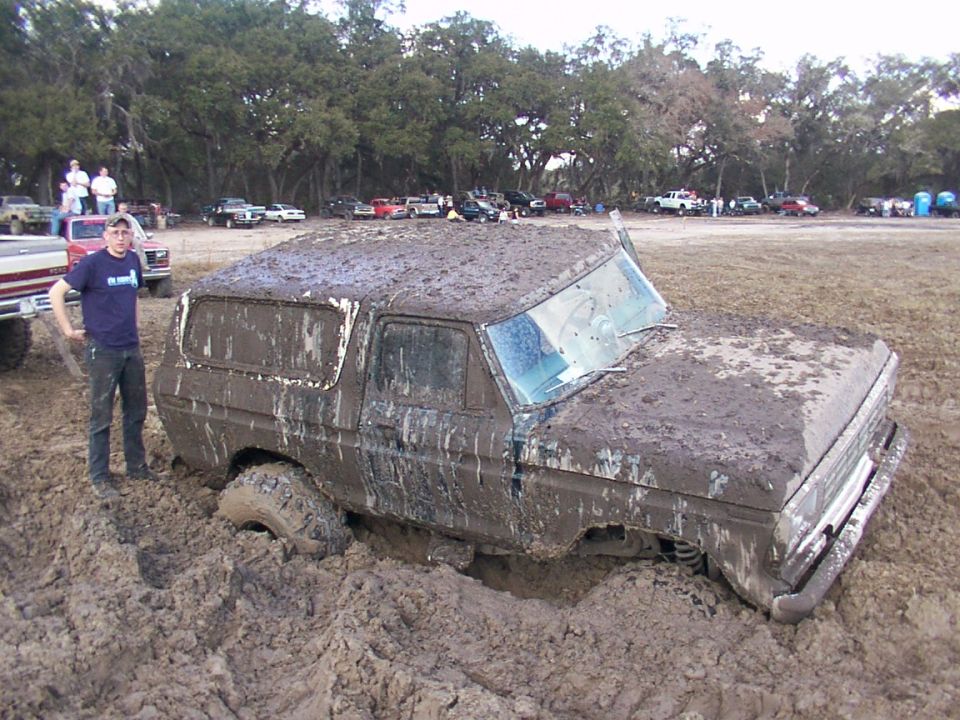 Mud-covered 1978 Ford Bronco stuck in mud pit with a person standing next to it