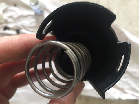 1978 Ford Bronco - A close-up view of a spring mechanism within a black housing, held by a person's hand.