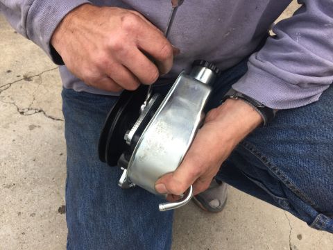 1978 Ford Bronco - A person works on a power steering pump, a component of a vehicle's steering system.