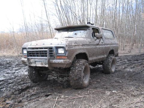 1979 Ford Bronco - This heavily muddied 1978 Ford Bronco is stuck off-road, its large tires digging into the wet terrain.