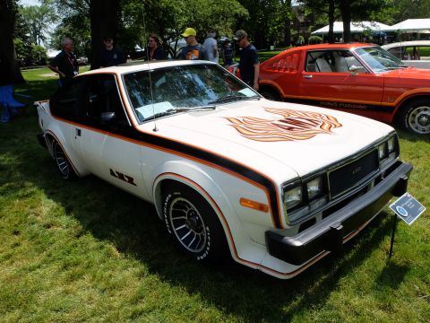 1971 Ford Ranchero - White 1978 AMC AMX with flame decal on hood and AMX badging on fender, parked on grass next to an orange car.