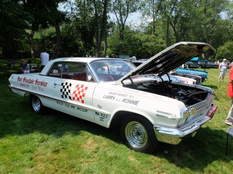 1971 Ford Ranchero - A classic white Chevrolet Impala with racing checkered flags and text is displayed outdoors with its hood up.